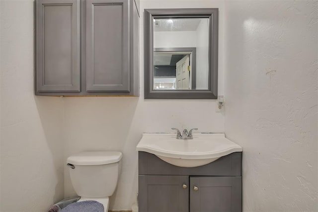 half bath featuring a textured wall, vanity, and toilet