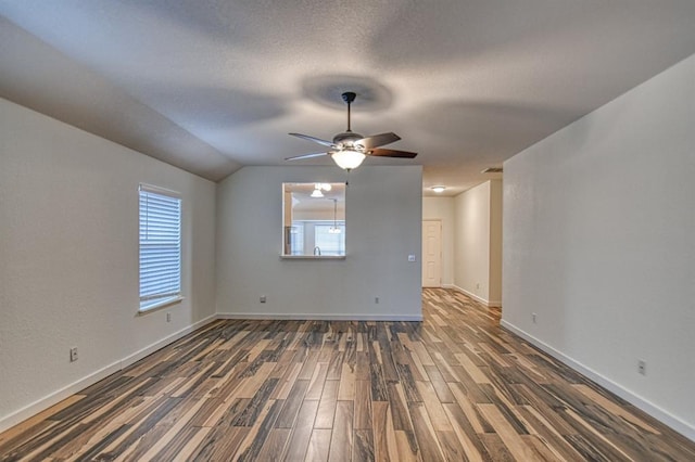 spare room featuring dark wood-type flooring, a ceiling fan, vaulted ceiling, a textured ceiling, and baseboards