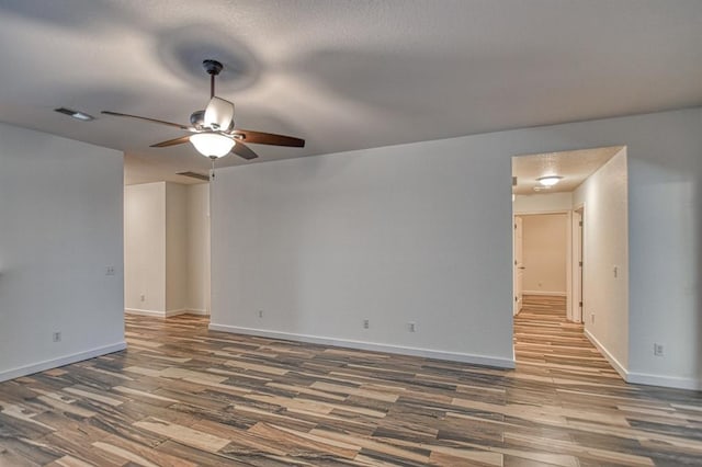 unfurnished room featuring a ceiling fan, visible vents, baseboards, and wood finished floors