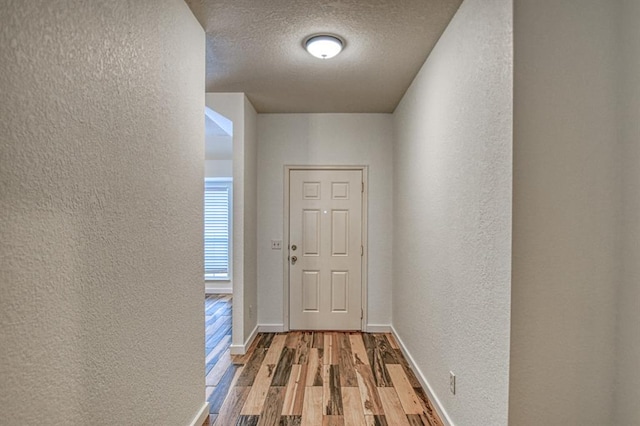 doorway to outside with a textured ceiling, baseboards, wood finished floors, and a textured wall