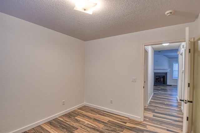 empty room with a fireplace with raised hearth, a textured ceiling, baseboards, and wood finished floors