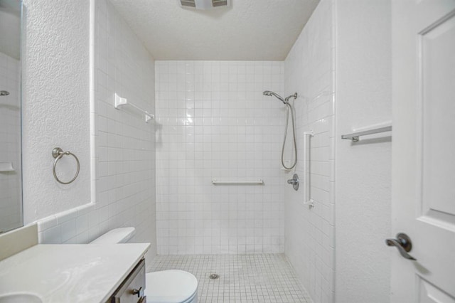 bathroom with tiled shower, vanity, toilet, and a textured ceiling