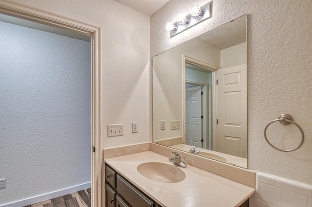 bathroom featuring a textured wall, vanity, baseboards, and wood finished floors