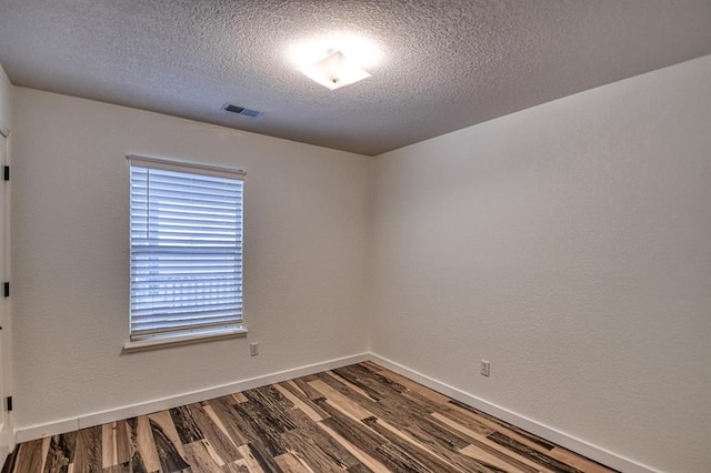 empty room with a textured ceiling, a textured wall, wood finished floors, visible vents, and baseboards