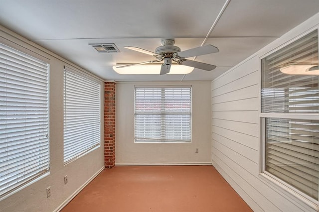 empty room with wood walls, visible vents, and a ceiling fan