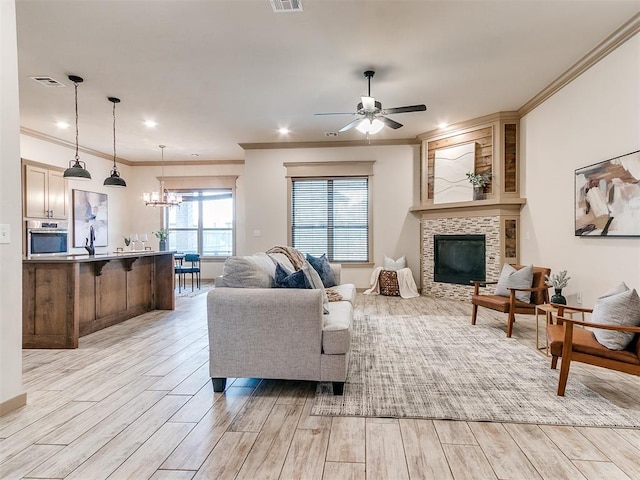 living area with a tiled fireplace, ceiling fan with notable chandelier, light wood-type flooring, and visible vents