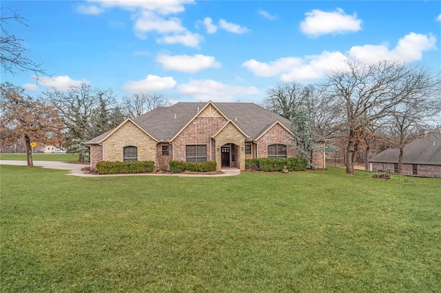 french provincial home with a shingled roof, a front yard, and brick siding