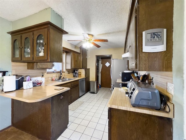 kitchen with a sink, a peninsula, appliances with stainless steel finishes, light countertops, and light tile patterned floors