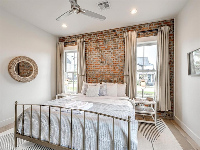 bedroom featuring visible vents, baseboards, brick wall, ceiling fan, and light wood-style floors