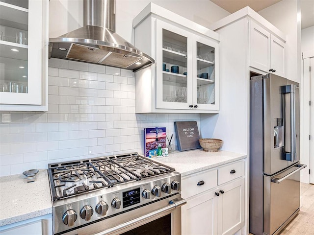 kitchen with stainless steel appliances, decorative backsplash, white cabinets, wall chimney range hood, and light stone countertops