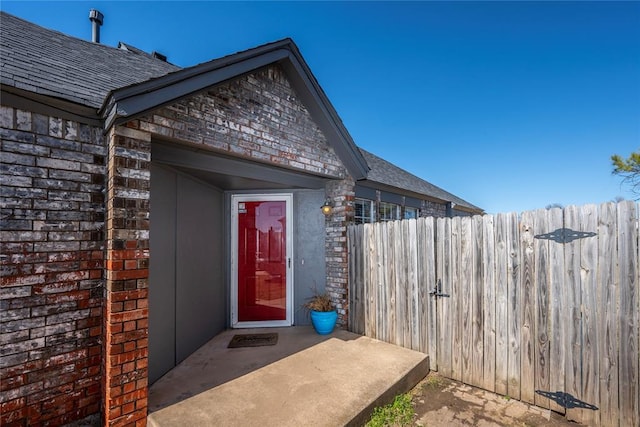 property entrance featuring a shingled roof, fence, and brick siding