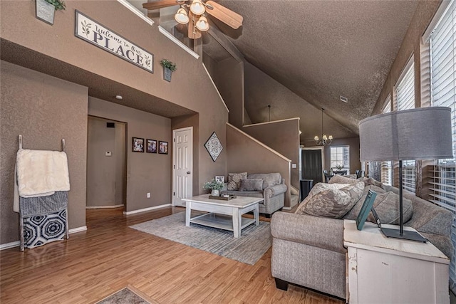 living room featuring a textured ceiling, high vaulted ceiling, ceiling fan with notable chandelier, and wood finished floors