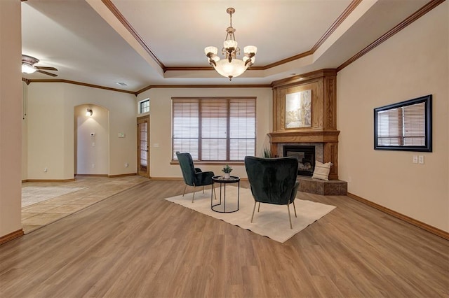 living area with light wood-type flooring, ceiling fan with notable chandelier, a tile fireplace, arched walkways, and a raised ceiling