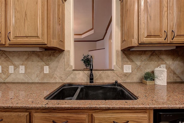 kitchen featuring light stone counters, decorative backsplash, ornamental molding, and a sink