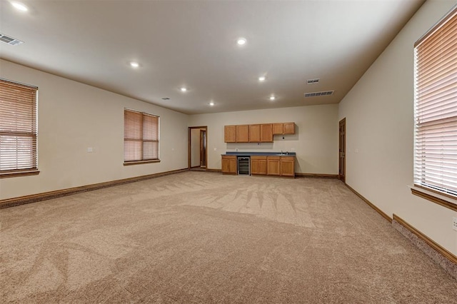 unfurnished living room featuring visible vents, wine cooler, light colored carpet, and baseboards