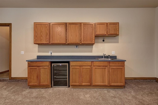 kitchen featuring beverage cooler, light colored carpet, dark countertops, and a sink