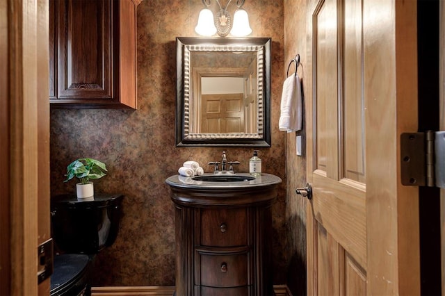 bathroom with a chandelier, toilet, wallpapered walls, and vanity