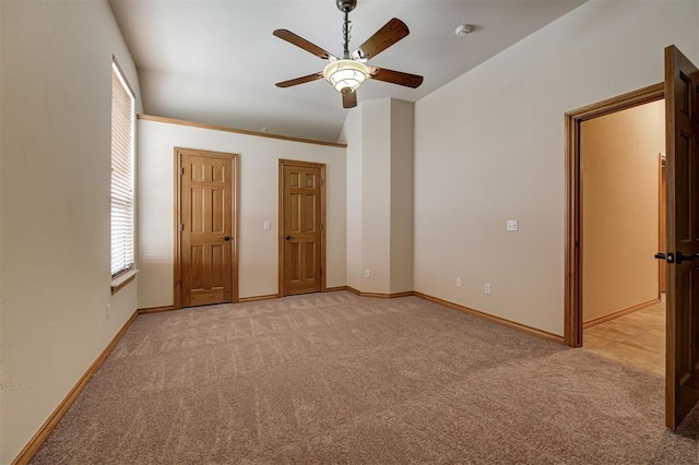 unfurnished bedroom with lofted ceiling, a ceiling fan, baseboards, and light carpet