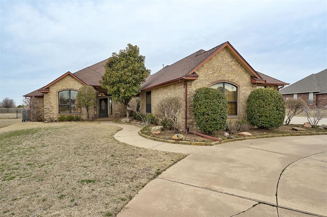 french country style house with brick siding, roof with shingles, and a front lawn