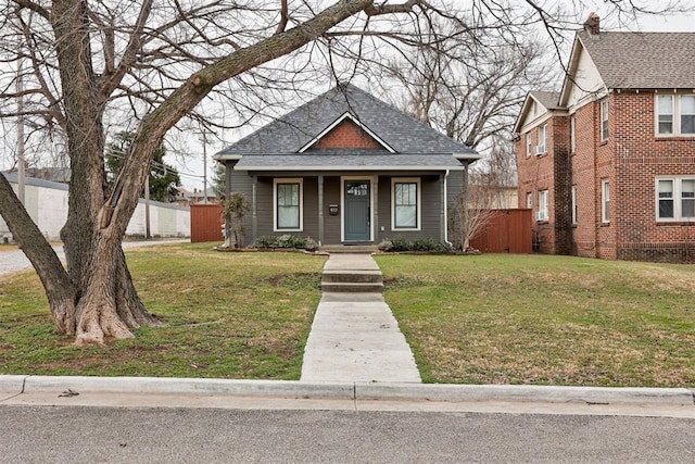 bungalow-style house featuring roof with shingles, fence, and a front yard