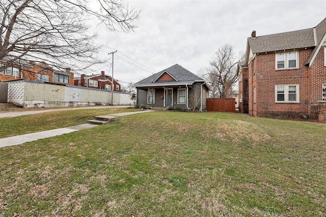 bungalow-style house with a shingled roof, fence, a front lawn, and brick siding