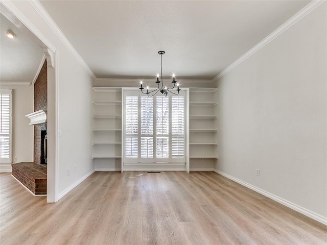 unfurnished dining area featuring a brick fireplace, a notable chandelier, crown molding, and wood finished floors