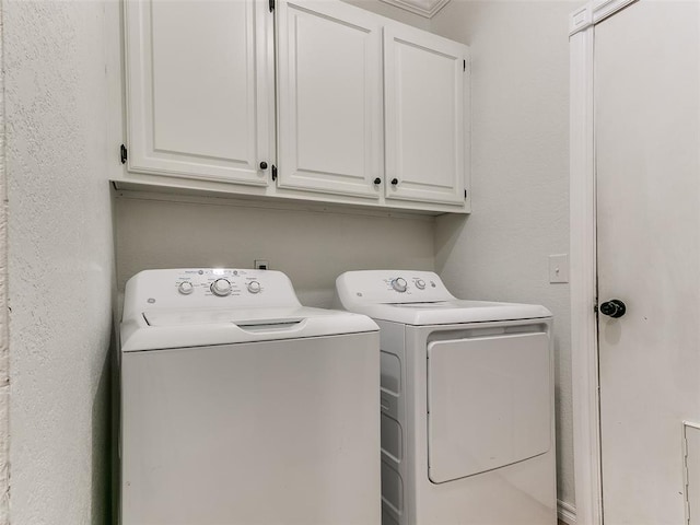 washroom featuring washer and dryer, cabinet space, and a textured wall