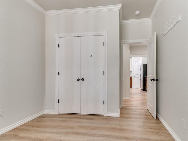 unfurnished bedroom featuring baseboards, light wood-style flooring, freestanding refrigerator, crown molding, and a closet