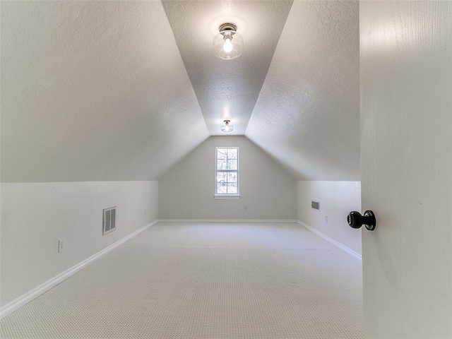 additional living space featuring a textured ceiling, carpet floors, visible vents, baseboards, and vaulted ceiling