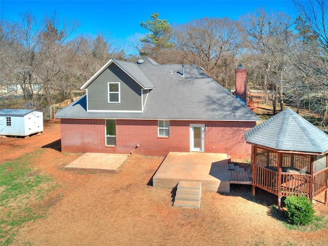 back of house with brick siding, a yard, roof with shingles, a gazebo, and a deck