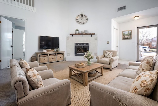 living area with visible vents, a fireplace with raised hearth, and a high ceiling