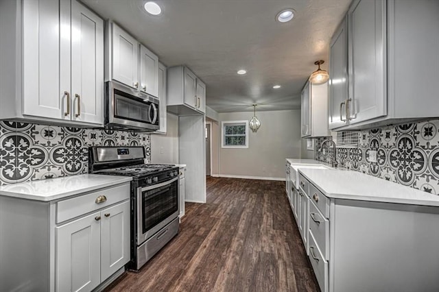 kitchen featuring stainless steel appliances, dark wood-type flooring, a sink, baseboards, and light countertops