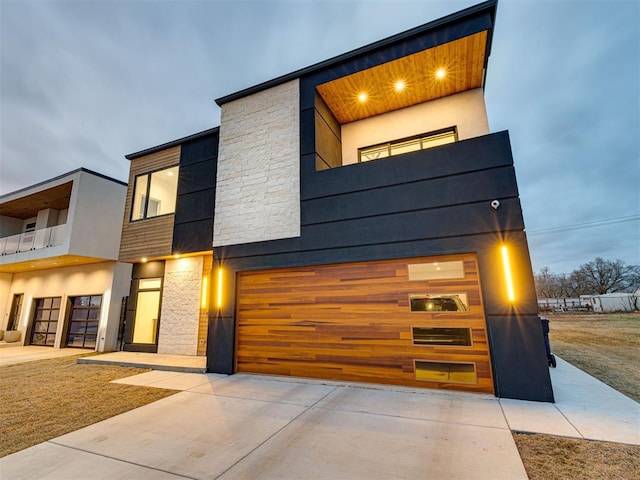 contemporary house featuring a balcony, stone siding, and driveway