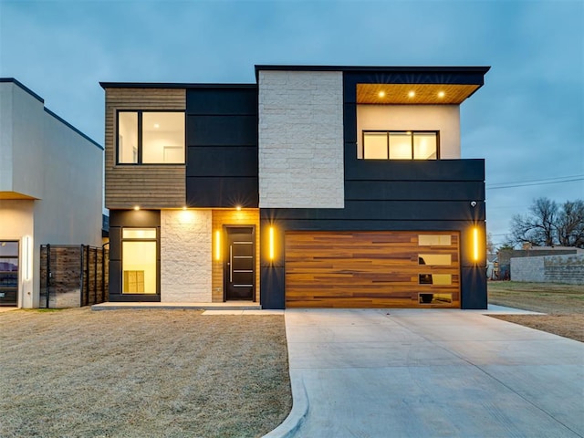 contemporary home with stone siding, a garage, and driveway