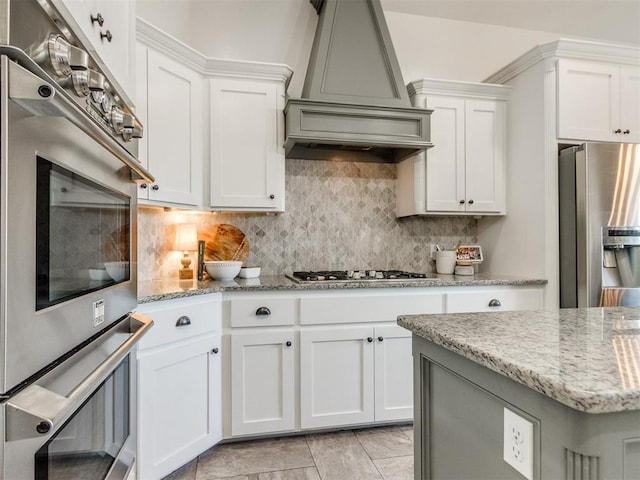 kitchen with decorative backsplash, white cabinetry, stainless steel appliances, and custom range hood