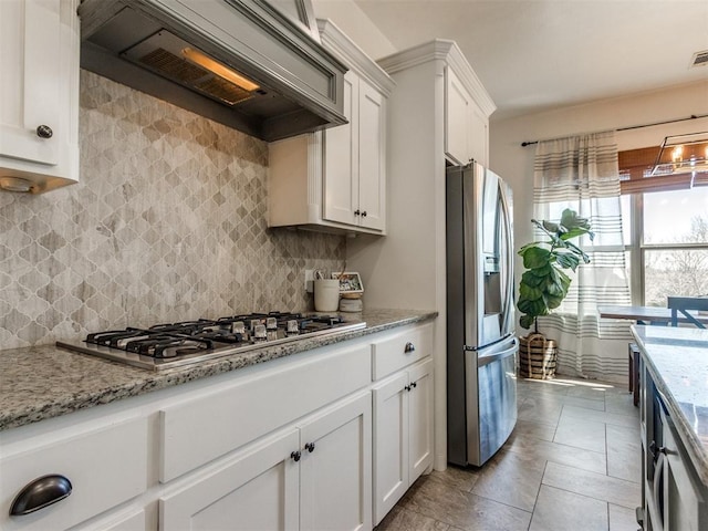 kitchen with premium range hood, light stone counters, decorative backsplash, appliances with stainless steel finishes, and white cabinets