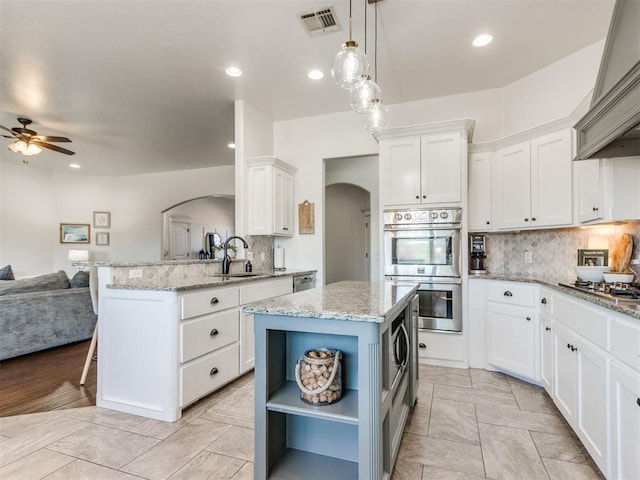 kitchen featuring premium range hood, a sink, open shelves, stainless steel appliances, and arched walkways