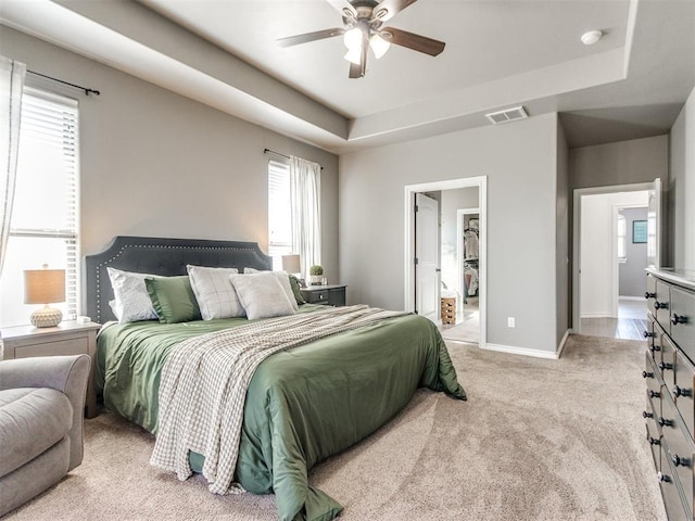 carpeted bedroom with a raised ceiling, baseboards, visible vents, and ceiling fan