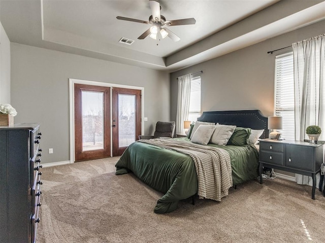 bedroom featuring visible vents, access to outside, a tray ceiling, french doors, and light colored carpet