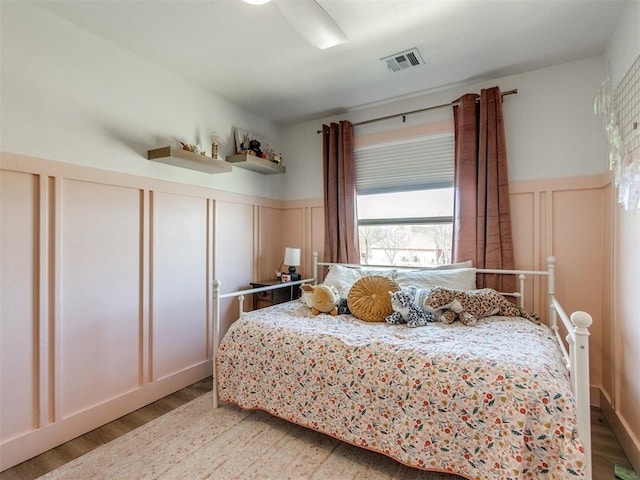 bedroom featuring a wainscoted wall, a decorative wall, wood finished floors, and visible vents