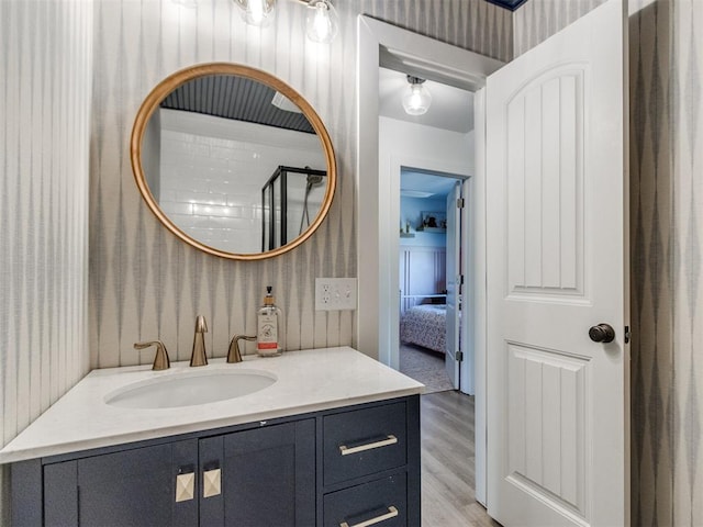 bathroom featuring wallpapered walls, wood finished floors, and vanity