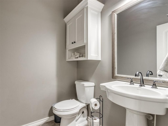 half bath with toilet, baseboards, and a sink