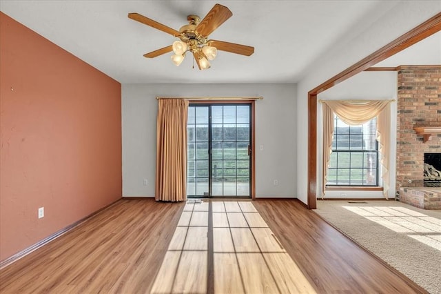 empty room with a brick fireplace, a healthy amount of sunlight, baseboards, and wood finished floors