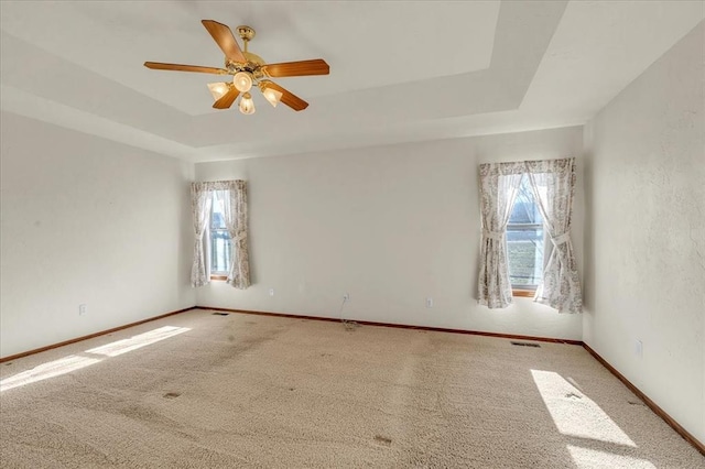 carpeted spare room featuring a tray ceiling, visible vents, ceiling fan, and baseboards