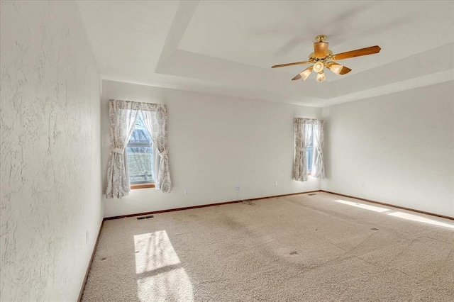 carpeted spare room with ceiling fan, a textured wall, visible vents, baseboards, and a raised ceiling