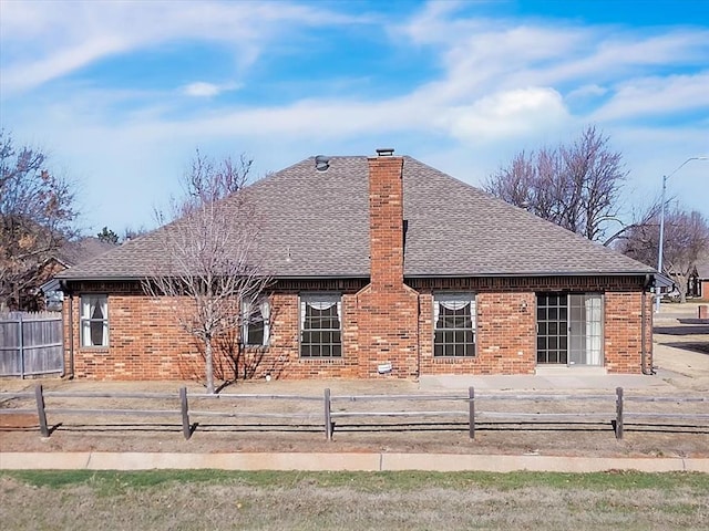 exterior space with a fenced front yard, roof with shingles, brick siding, and a chimney