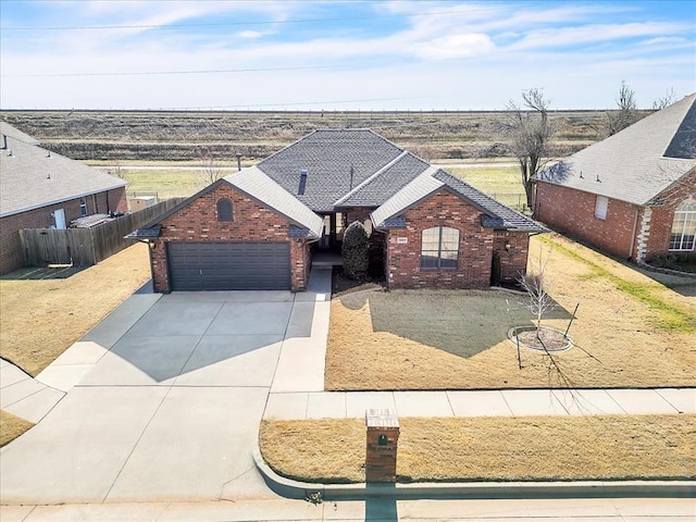 view of front of property featuring driveway, a shingled roof, an attached garage, fence, and brick siding