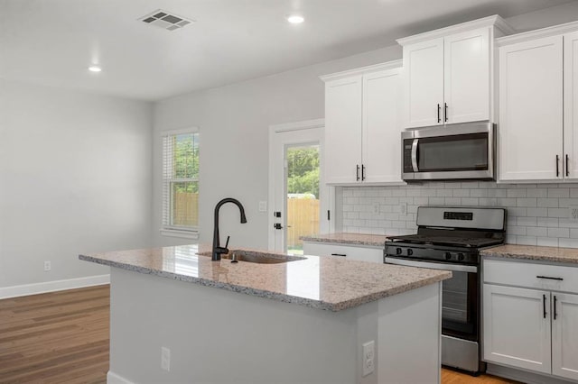 kitchen with stainless steel appliances, a sink, visible vents, decorative backsplash, and a center island with sink