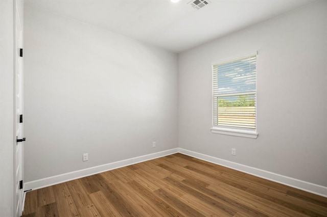 spare room featuring wood finished floors, visible vents, and baseboards