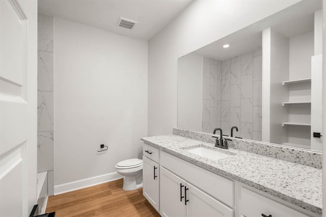 bathroom featuring visible vents, toilet, vanity, wood finished floors, and baseboards